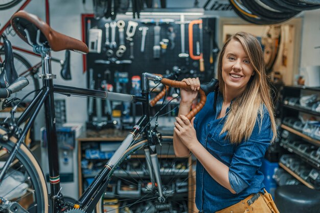 女性の自転車のメカニックは、ワークショップで自転車を修復しています