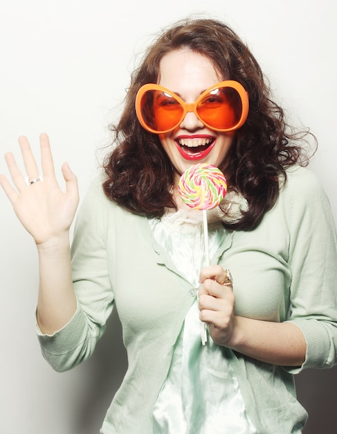 woman in big orange glasses licking lollipop with her tongue