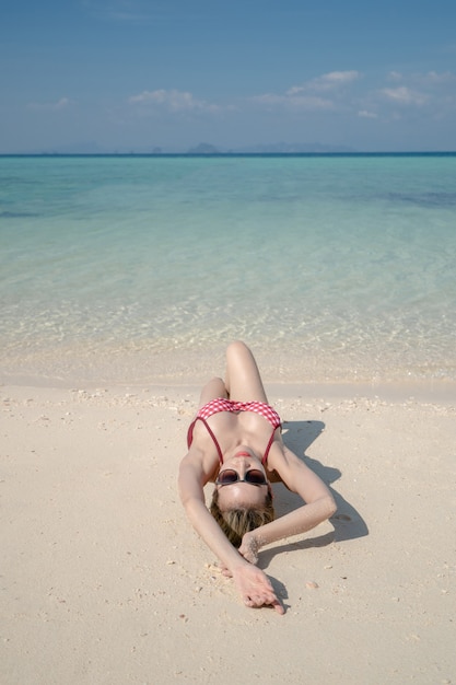 白い砂浜のそばの海の水の上に横たわっているビキニの女性。青い海と空の風景。夏休み。