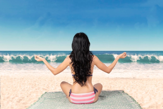 Женщина в бикини медитирует на пляже