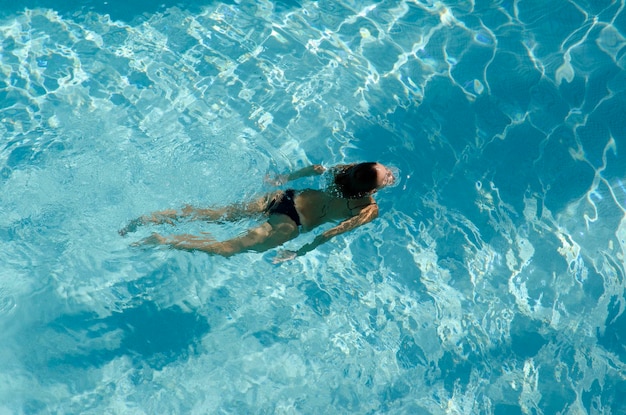 Woman in bikini swimming in crystal clear water in a blue colored pool top view