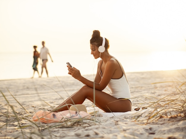 Woman in Bikini with a Smartphone and Headphones on the Beach