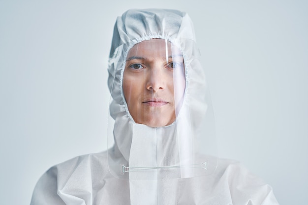 Woman in bio-hazard suit and face shield on white background.