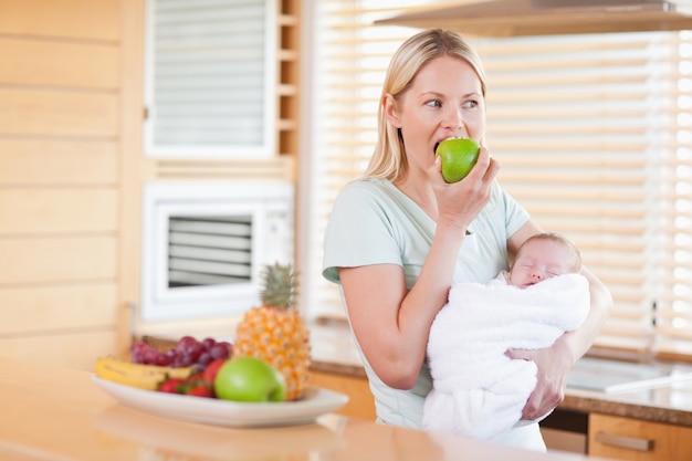 Donna che morde nella mela con il bambino sulle sue braccia