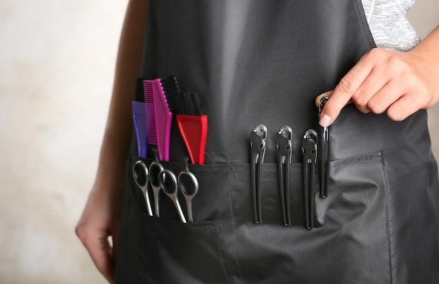 Woman in black apron with professional hairdresser set on light background closeup
