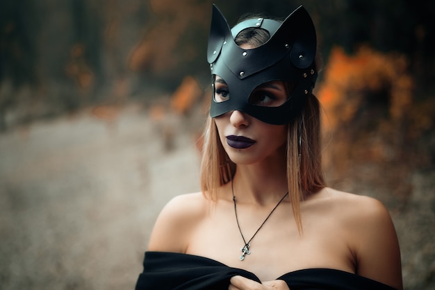 A woman in a black cat mask stands on the background of nature.