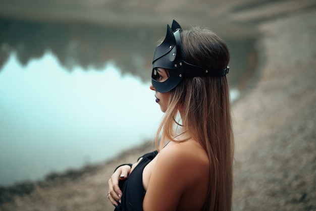 A woman in a black cat mask stands on the background of nature.