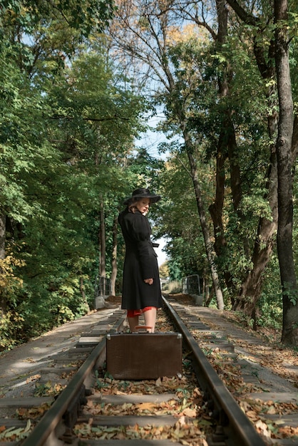 Woman in the black coat has left the suitcase on the rails and is leaving Autumn forest