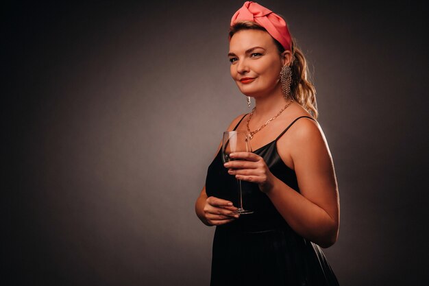 A woman in a black dress holding a glass of champagne on a black background, Christmas, holiday