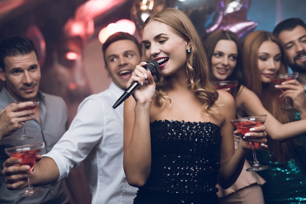 Photo woman in black dress is singing songs with her friends.