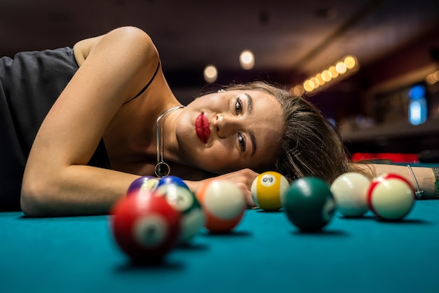 Woman in black dress near balls lying on snooker table