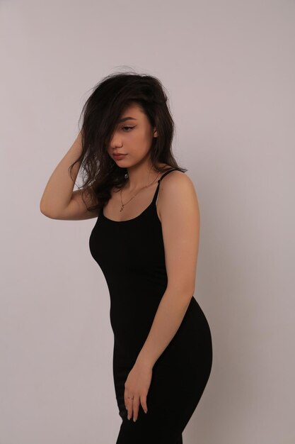 a woman in a black dress poses in front of a white wall