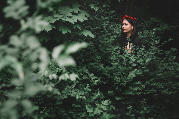 숲의 배경에 그녀의 손에 나뭇가지를 들고 검은 드레스와 붉은 장식의 여자