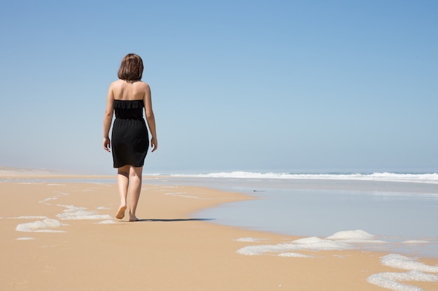 Woman on black dress walk on the beach