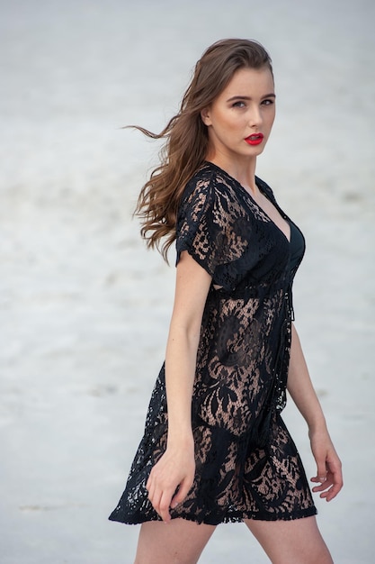 A woman in a black dress walks on the beach