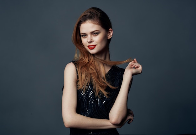 a woman in a black dress with red hair on a gray background gestures with her hands