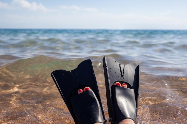 검은 오리발을 입은 여성이 해안 근처에서 튀었습니다. 지느러미가 물 밖으로 튀어나옵니다. 수영 장비.