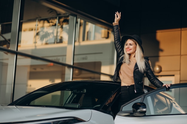 Donna con cappello nero in piedi accanto alla sua nuova macchina bianca