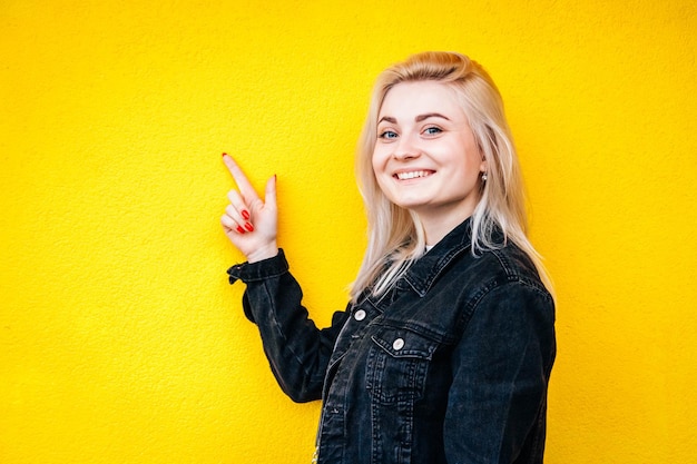 Woman in black jacket smiling while lifting a finger up posing against a background of yellow