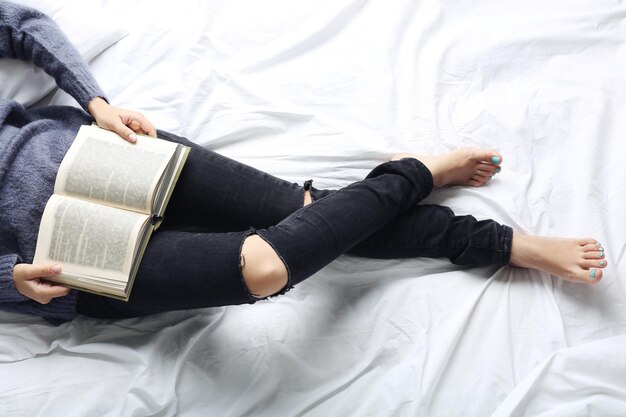 Woman in black jeans reading book on bed top view point