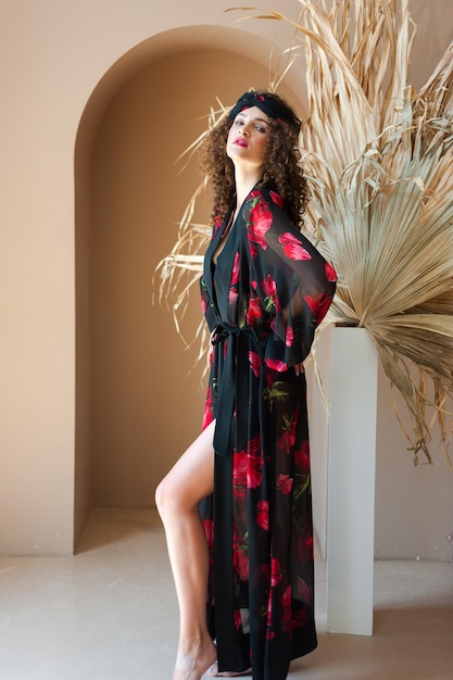 A woman in a black kimono stands in front of a plant