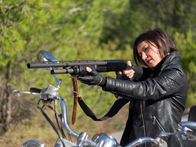 A woman in a black leather biker jacket with a carbine rifle on a chopper motorcycle in Greece