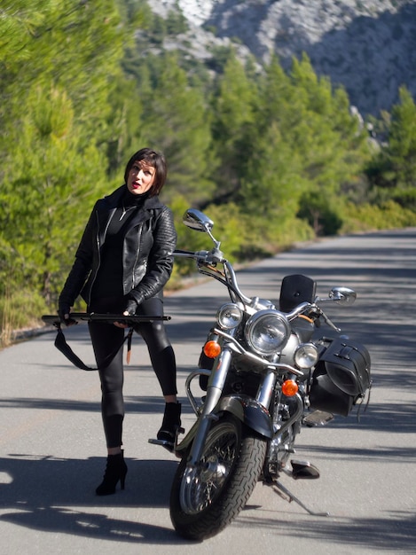 A woman in a black leather biker jacket with a carbine rifle on\
a chopper motorcycle in greece