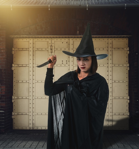 Woman in Black Scary witch halloween costume, Holding a knife with Brick Wall of the Ancie