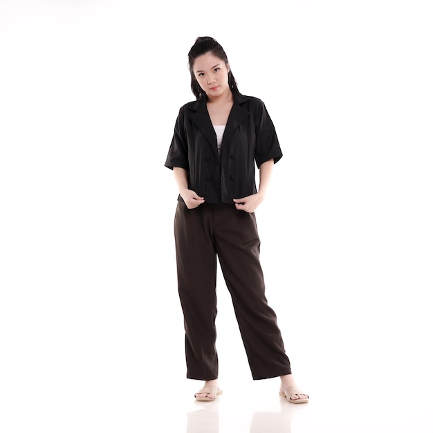 A woman in a black shirt and brown pants stands in front of a white background.