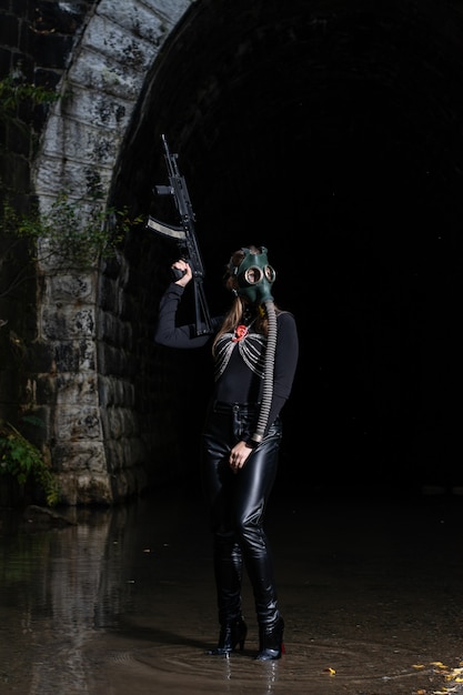 A woman in a black suit and gas mask with a machine gun in her hands