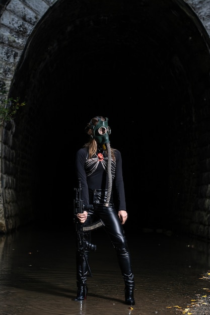 A woman in a black suit and gas mask with a machine gun in her hands