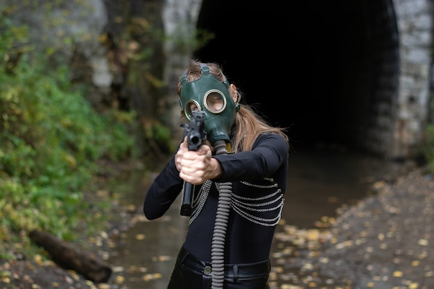 A woman in a black suit and gas mask with a machine gun in her hands