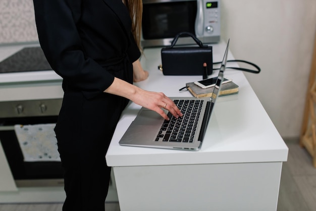 Woman in black suit smiling at the laptop in kitchen