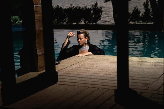 黒いスーツを着た女性がプールに立ち、髪が風になびいている。