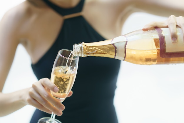 Woman in black swimsuit is pouring sparkling wine into a glass