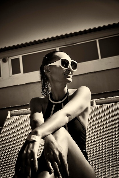 Woman in a black swimsuit and white sunglasses sunbathing on a sunbed