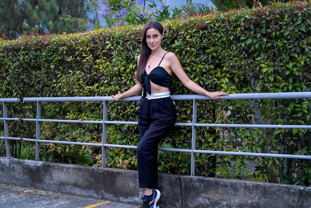 A woman in a black top and black pants stands on a metal fence.