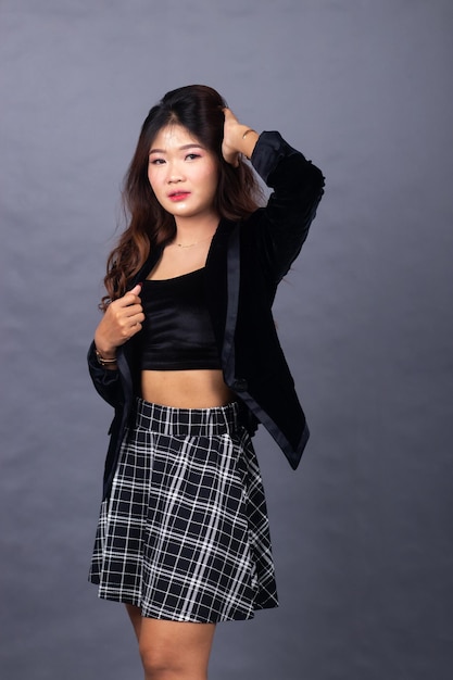 A woman in a black top and plaid skirt stands in front of a grey background