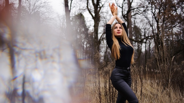 Foto donna in pantaloni neri e maglione in piedi sul campo di spighette essiccate mani in alto