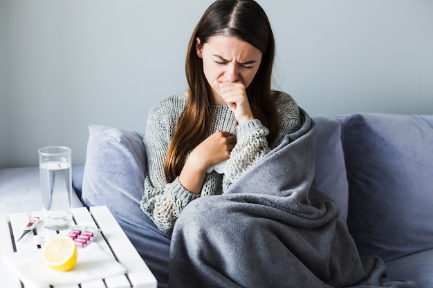 Woman under blanket coughing 