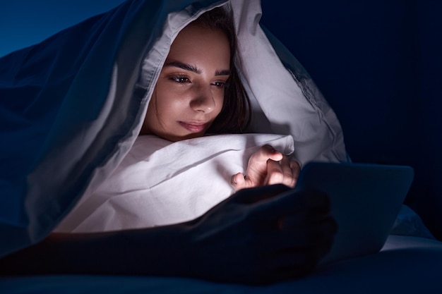 Woman under blanket using tablet at night