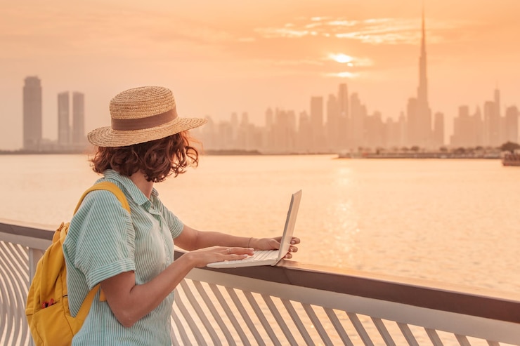 Photo woman blogger or copywriter or student works and studies using a laptop and admires the colorful sunset over dubai creek with a view of the skyscrapers and the burj khalifa