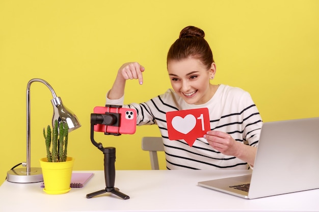 Woman blogger recording video for followers holding like sign asking to rate her posts and subscribe