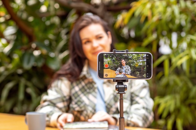 A woman blogger records herself on a smartphone camera standing on a tripod Freelancer communication via the Internet