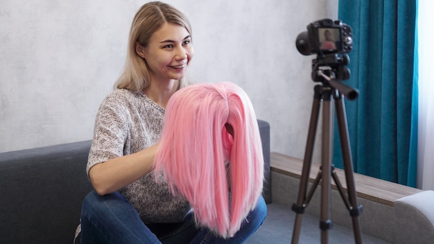 Женщина-блогер записывает видео. Она рассказывает о стрижках и показывает розовый парик. Стилист и консультант по моде записывают лекцию