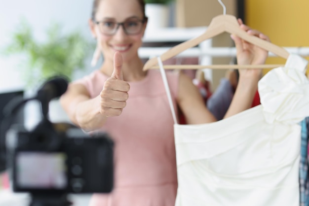 Женщина-блоггер показывает палец вверх и держит платье перед камерой крупным планом онлайн-продажа