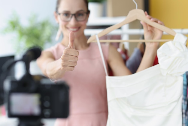 Woman blogger showing thumb up and holding dress in front of camera closeup online sale of