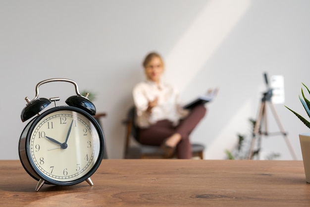 Woman blogger video webinar on background closeup of alarm clock selective