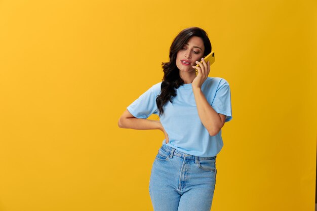 Woman blogger with a phone in her hands in a blue t-shirt and jeans on a yellow background smile