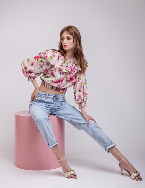 Woman in blouse top with floral pattern in red blue jeans Model sitting on pink cube cylinder